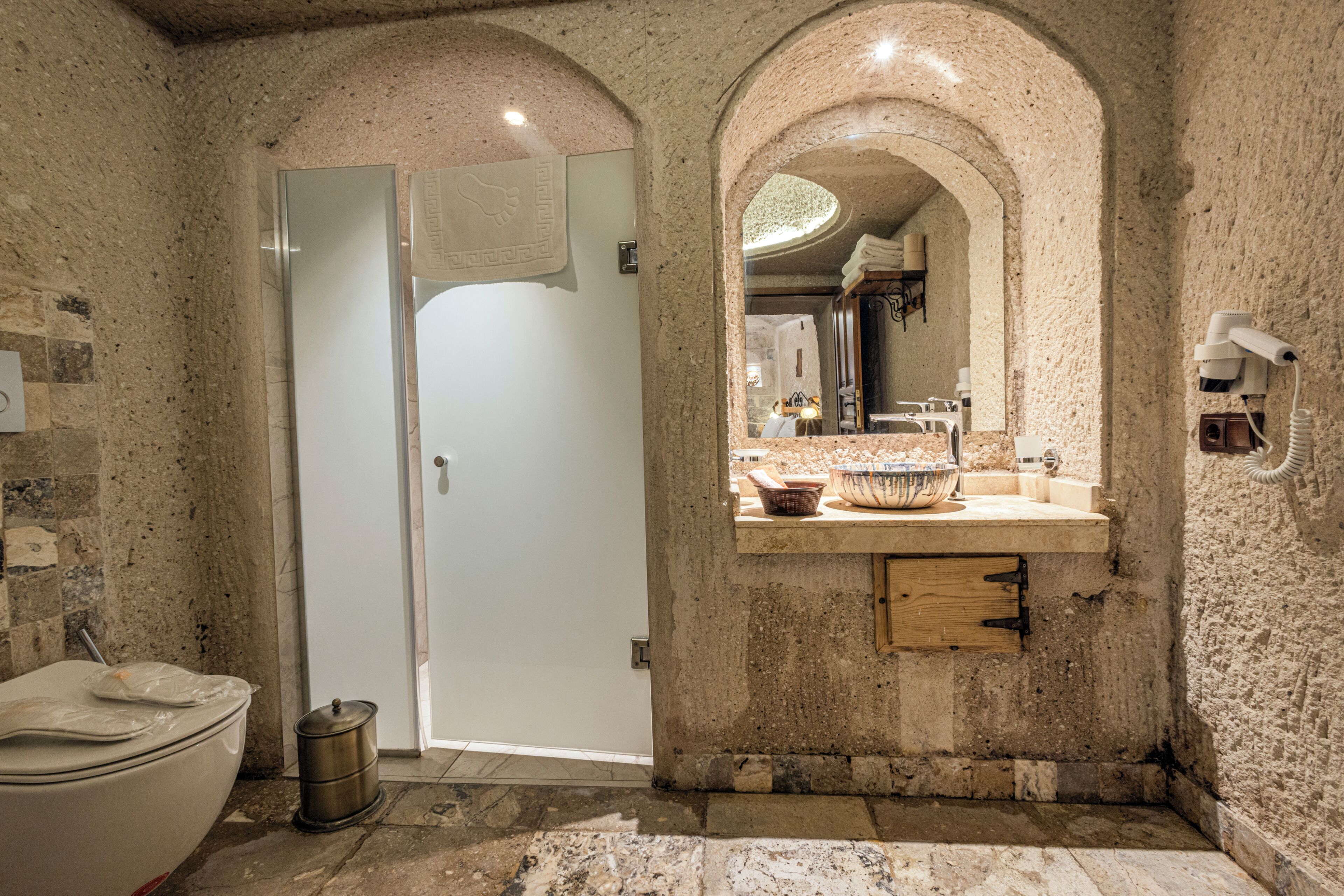 A bathroom with a stone wall, a sink with a bowl, a mirror, and a toilet.