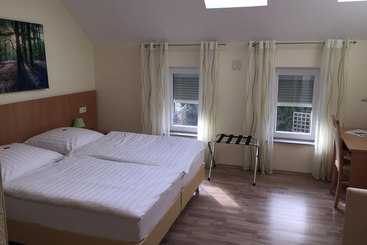 A bedroom with a bed, a desk, and two windows with curtains.