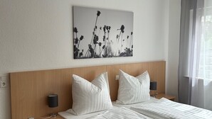 A hotel room with a wooden headboard, a large bed with white bedding, two bedside tables with lamps, and a wall-mounted artwork of flowers. - Pension im Wirtshaus Himberg (Bad Honnef)