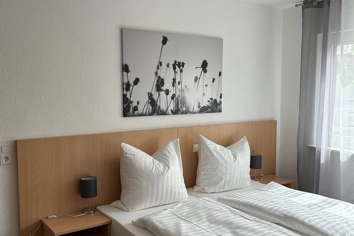 A hotel room with a wooden headboard, a large bed with white bedding, two bedside tables with lamps, and a wall-mounted artwork of flowers.