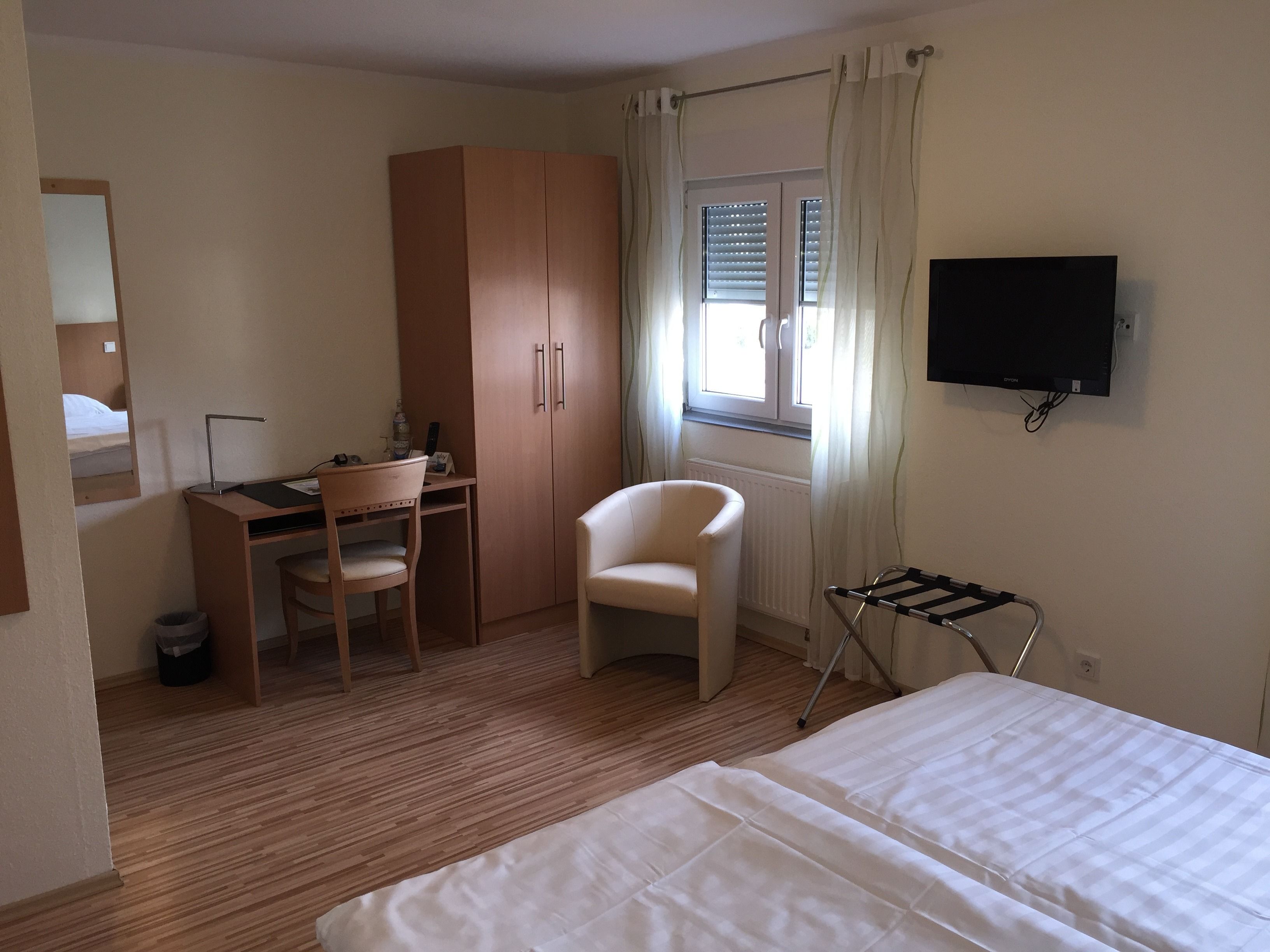 A hotel room with a bed, a desk with a chair, a wardrobe, a TV, and a window with curtains.