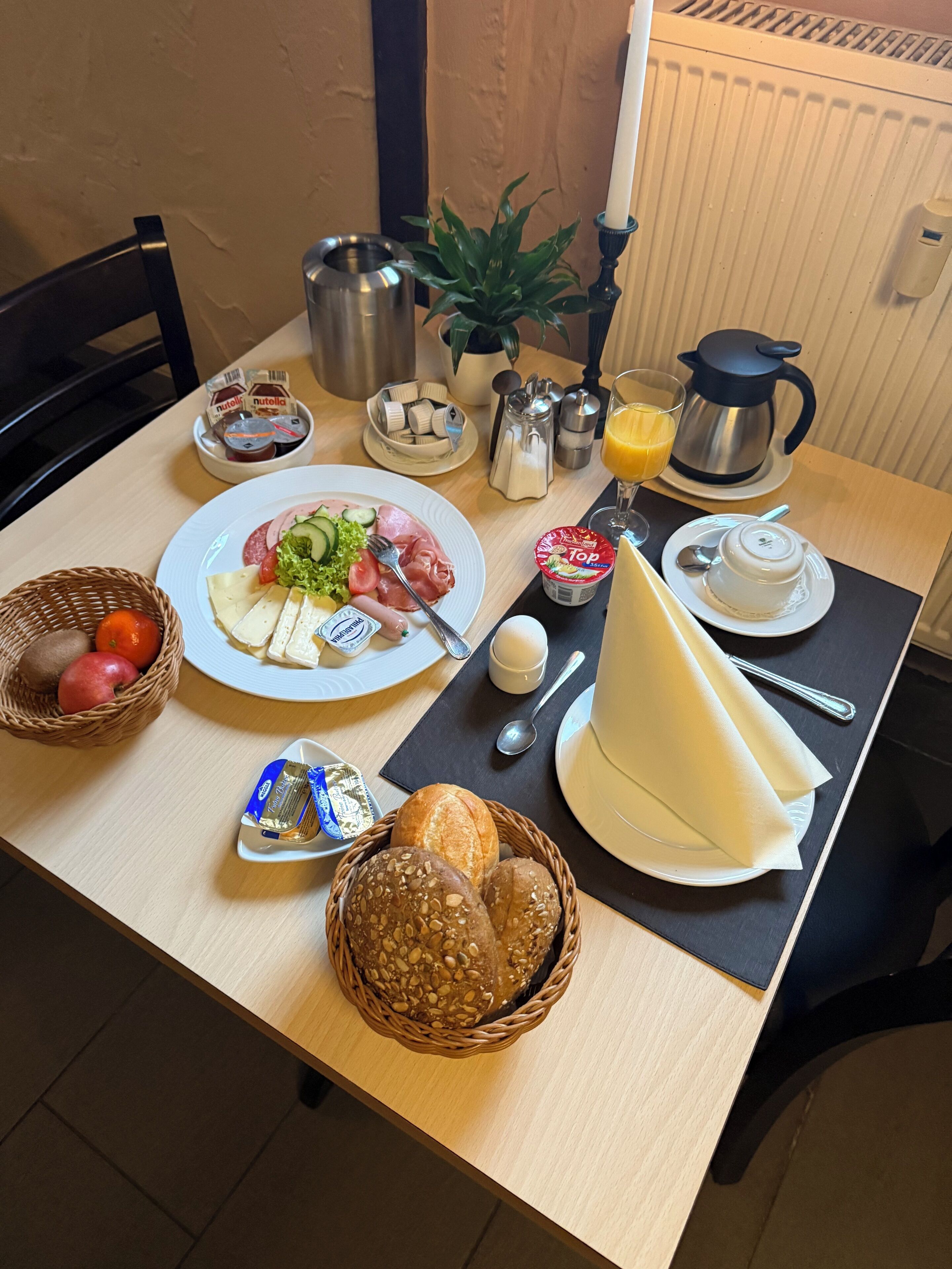 Ein Esstisch mit Speisen, einer Kaffeekanne, einem Orangensaftkrug und einer Pflanze.