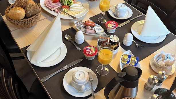 A breakfast table set with various food items, including bread, eggs, and fruit. - Pension im Wirtshaus Himberg (Bad Honnef)