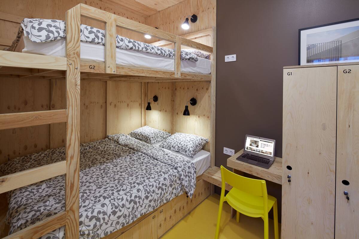 Une chambre avec un lit superposé, un ordinateur portable posé sur un bureau et une chaise jaune.
