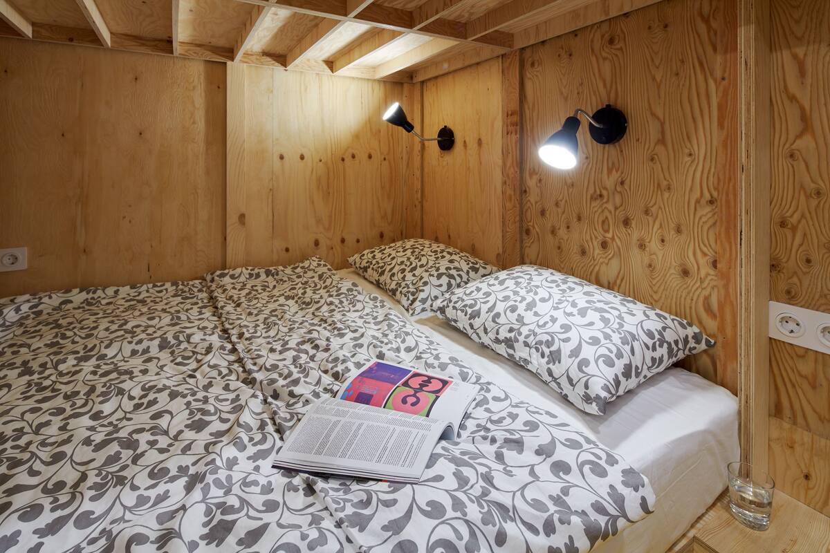 Une pièce aux murs lambrés, avec un lit, deux lampes fixées au mur et un magazine posé sur le lit.