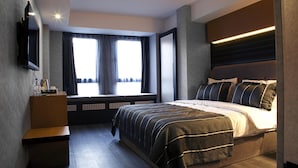 A modern bedroom with a large bed, a bedside table, a flat-screen TV mounted on the wall, and a window with curtains. - The Black Hotel (Eskisehir)