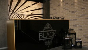 A reception desk with a black and gold design, a staircase, and a brick wall in the background. - The Black Hotel (Eskisehir)