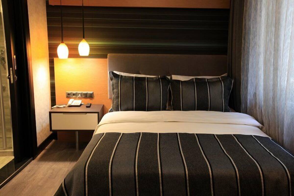Ein Hotelzimmer mit einem großen Bett, einem Nachttisch mit Telefon und Fernbedienung sowie zwei Pendelleuchten.