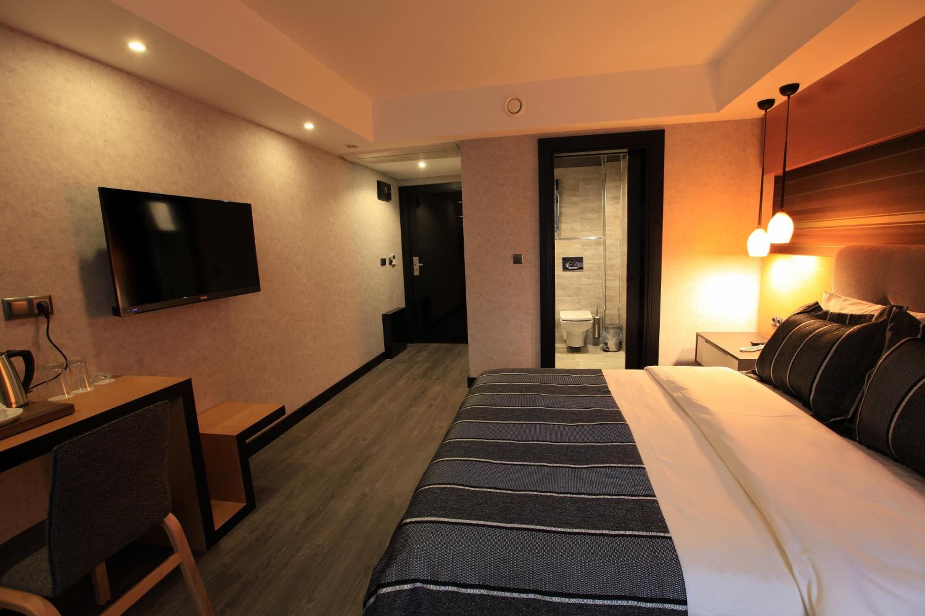 Une chambre d’hôtel comprenant un lit, un bureau avec une chaise, un téléviseur fixé au mur et une salle de bain visible à travers une porte ouverte.