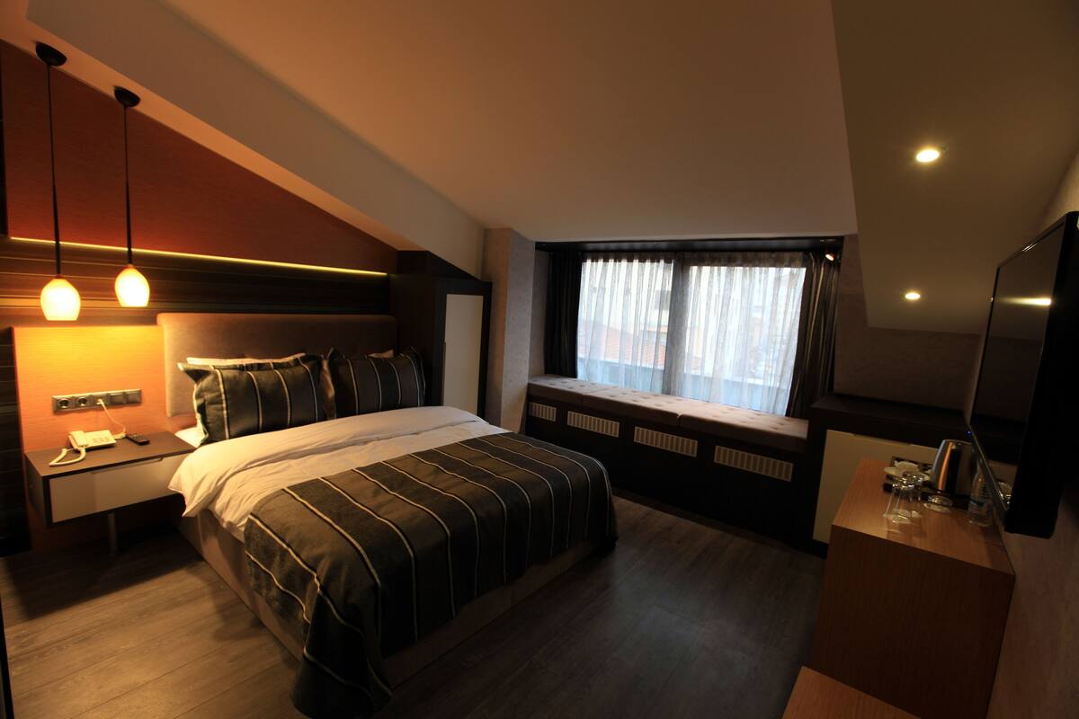 Ein modernes Hotelzimmer mit einem großen Bett, Nachttischen, einem Fenster mit Vorhängen und einem Fernseher auf einem Schrank.