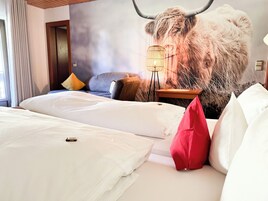 Habitación de hotel con un gran mural de un toro, cama con sábanas blancas, almohada roja y una lámpara de pie.