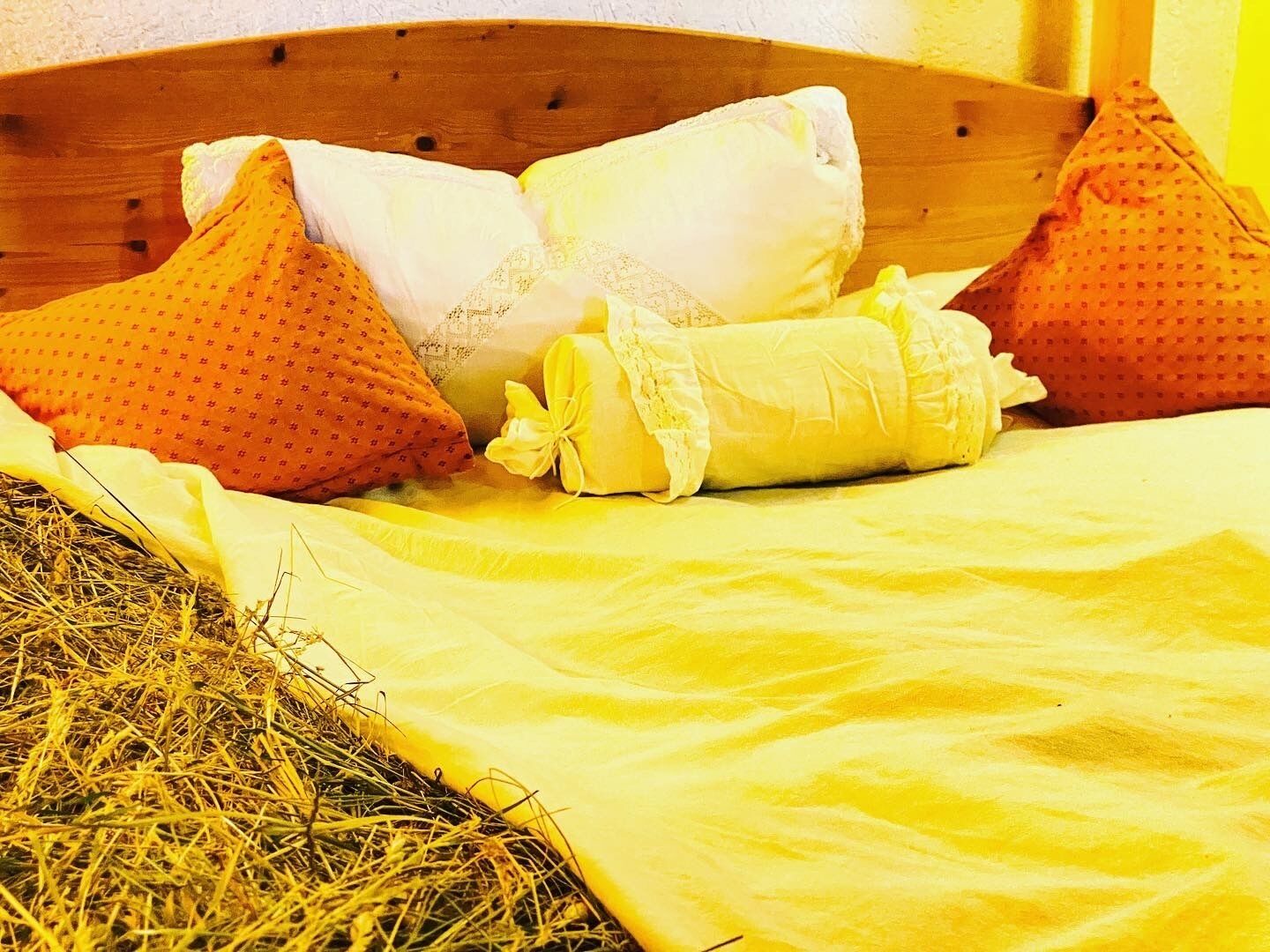 A bed with a yellow bedspread, two pillows, and a rolled-up blanket.