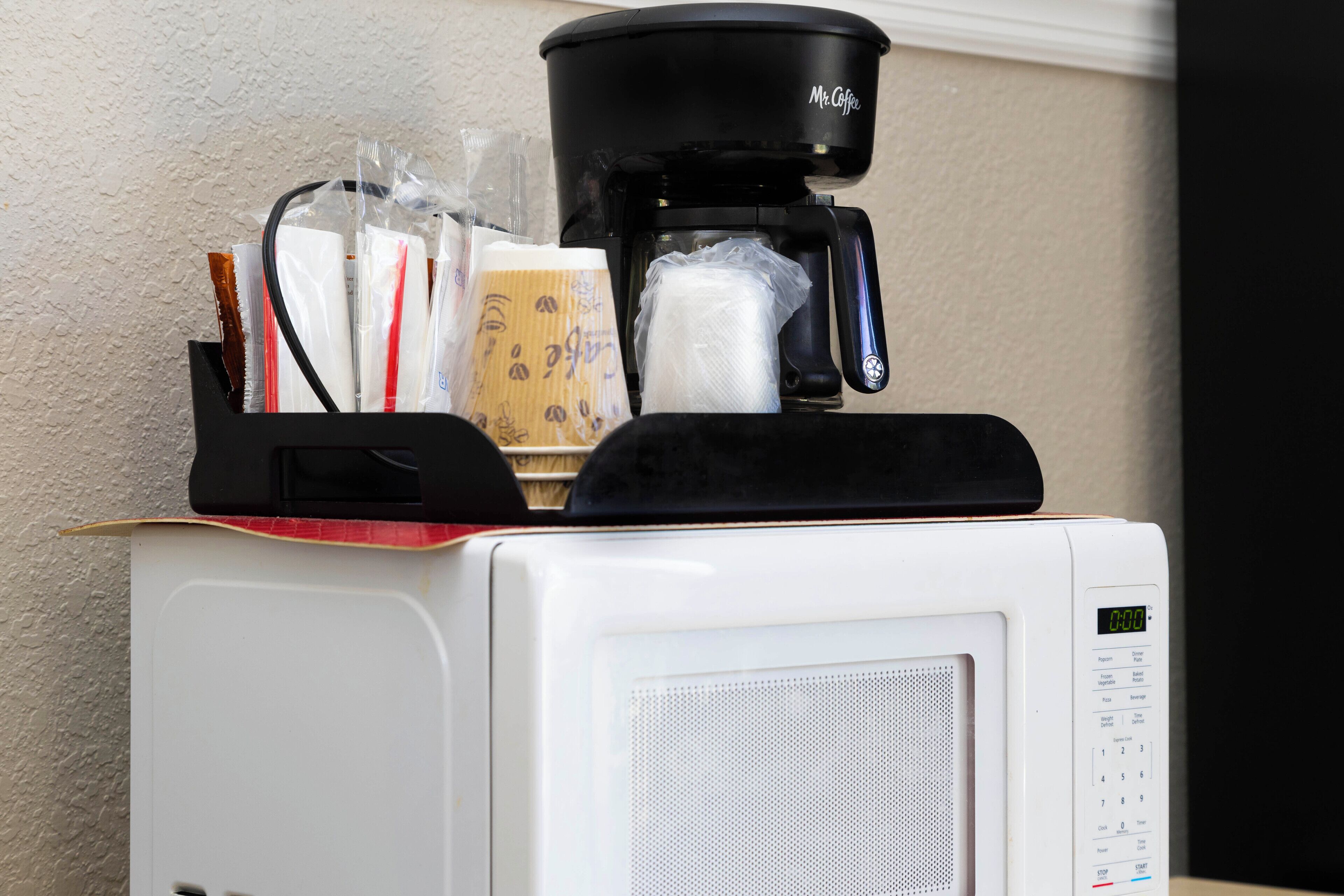 Un four à micro-ondes sur lequel est posée une machine à café, contenant une cafetière, un sachet de dosettes de café et un sac en papier.