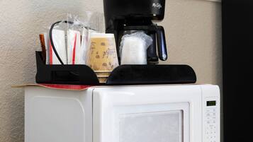 Un four à micro-ondes sur lequel est posée une machine à café, contenant une cafetière, un sachet de dosettes de café et un sac en papier.