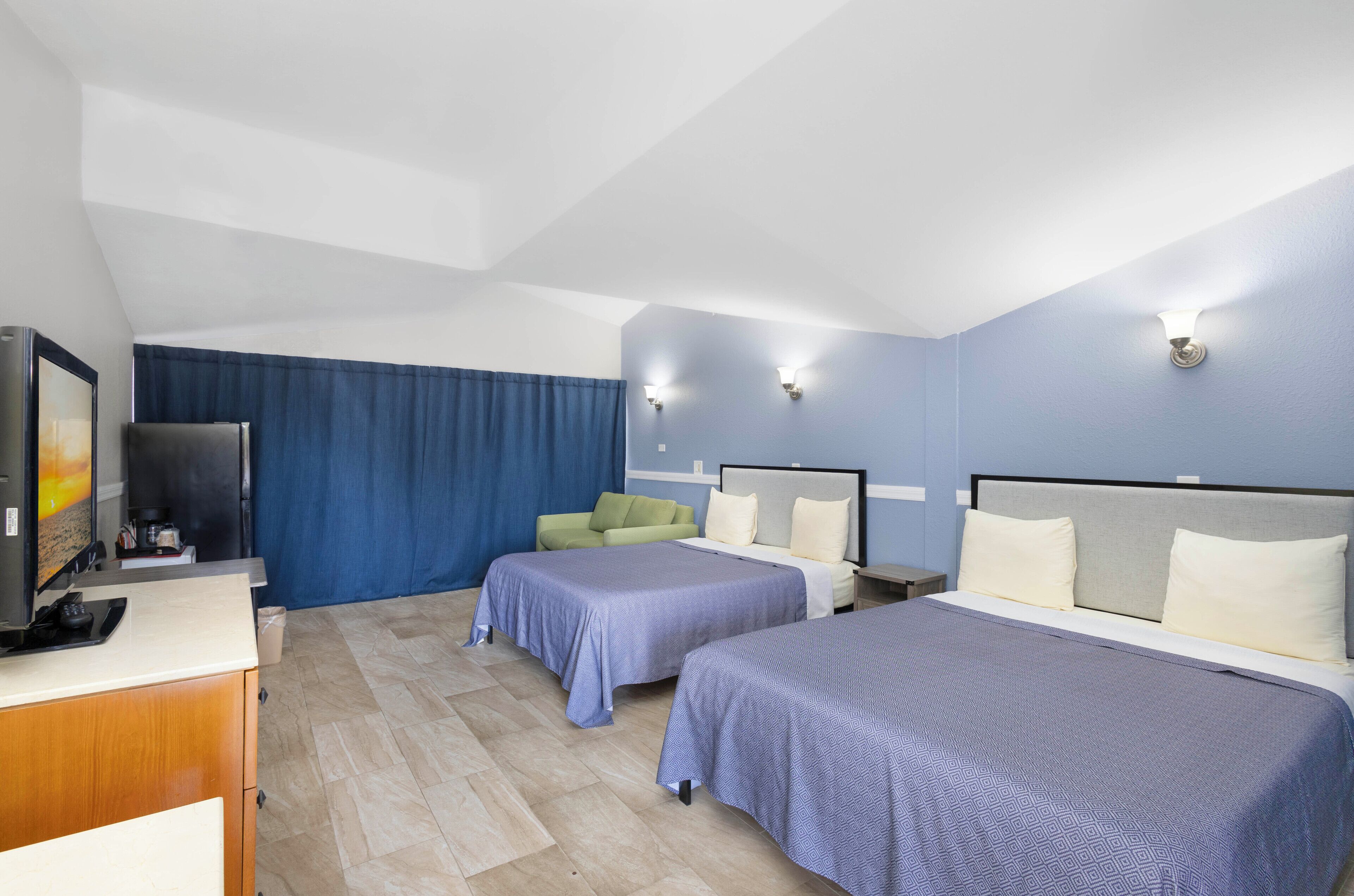Habitació d'hotel amb dos llits, una taula de treball, una televisió i una cortina blava.