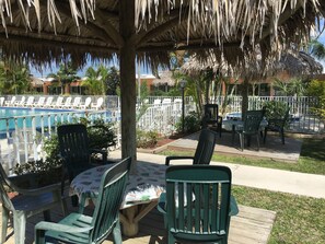 A poolside area with lounge chairs and a table under a thatched roof. - Warm Mineral Springs Motel (North Port)