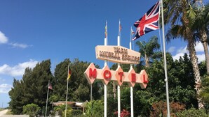 A motel sign with flags, surrounded by greenery and palm trees. - Warm Mineral Springs Motel (North Port)