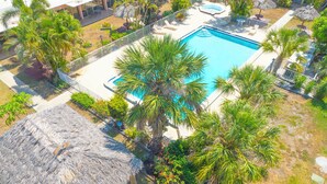 An aerial view of a resort with a swimming pool surrounded by palm trees and a thatched-roof structure. - Warm Mineral Springs Motel (North Port)