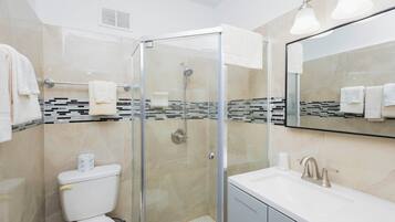 Une salle de bain moderne dotée d’une douche à parois de verre, de toilettes, d’un lavabo avec un miroir et d’un mur recouvert de carreaux.