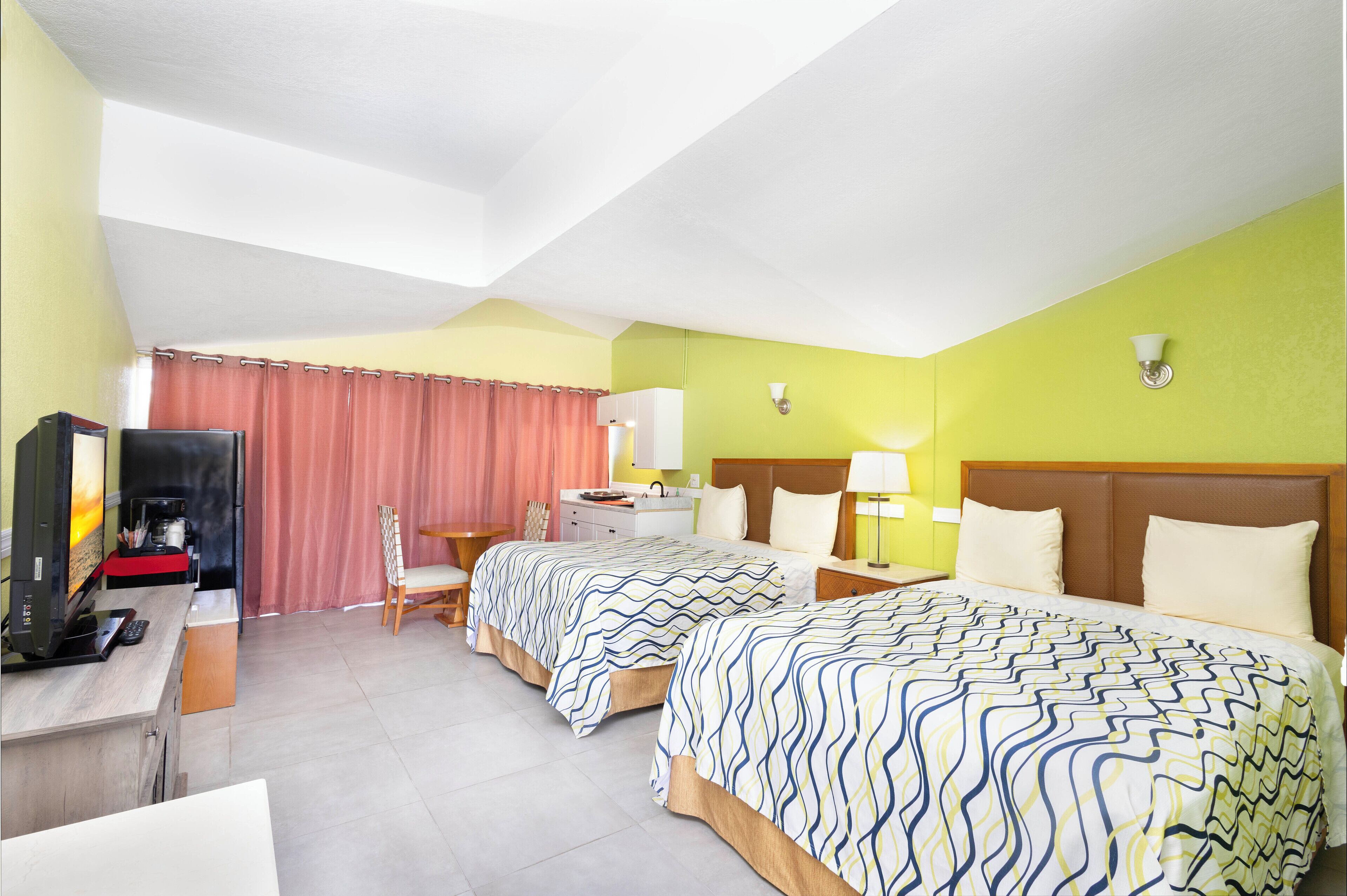 A hotel room with two beds, a desk with a computer, a coffee maker, and a TV.