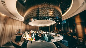 Un espace bar moderne doté d’un comptoir circulaire, de sièges et d’un grand luminaire décoratif au plafond.