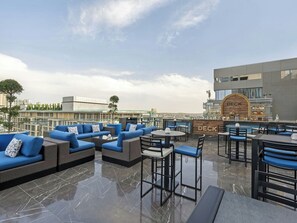 Un bar en la azotea con asientos y barra, con vistas a un paisaje urbano.