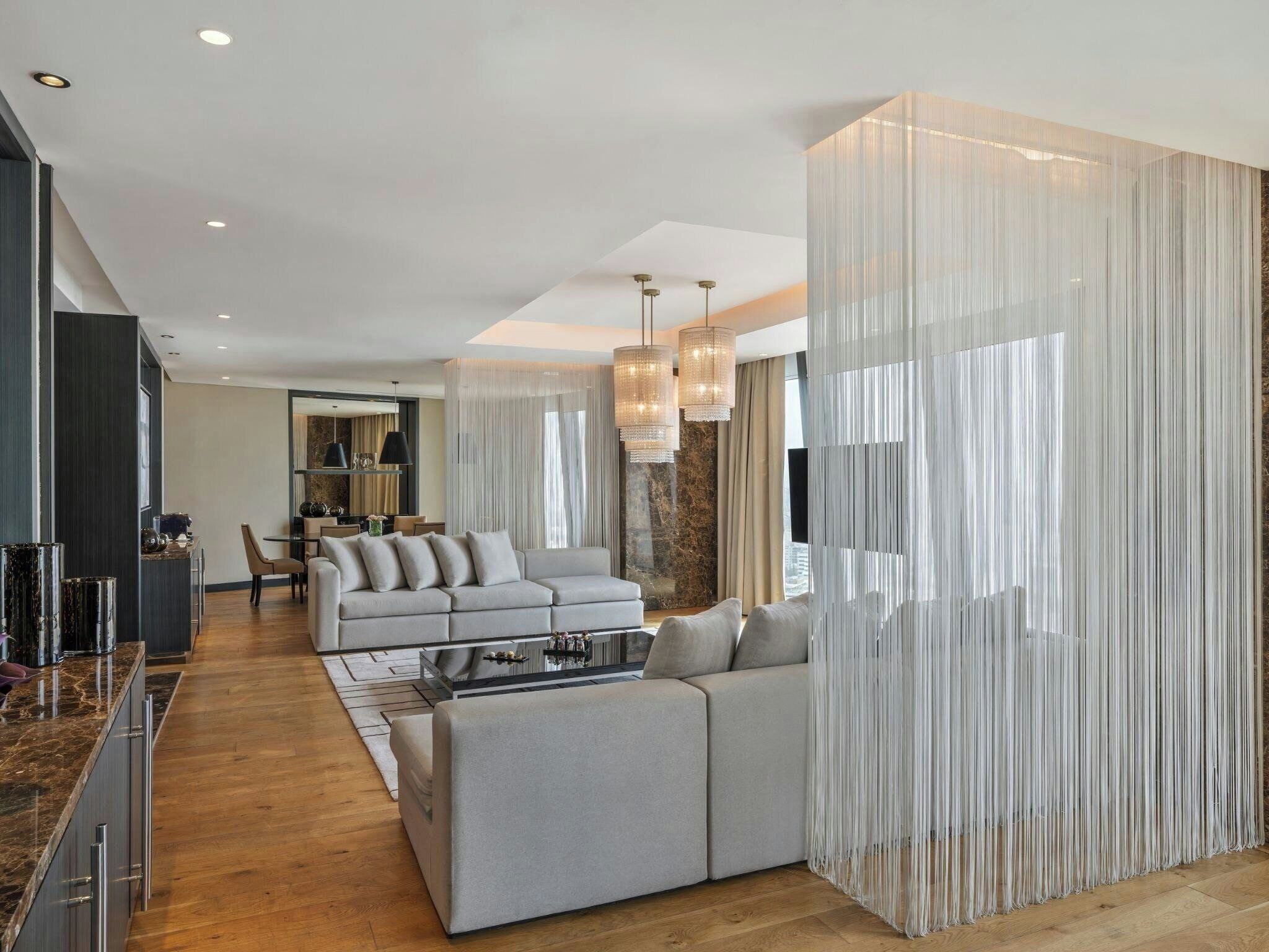 A modern living room with a sofa, a coffee table, and a dining area in the background.