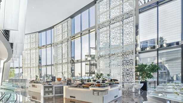 Un hall d’hôtel moderne avec un comptoir d’accueil central, de grandes fenêtres et un sol réfléchissant.