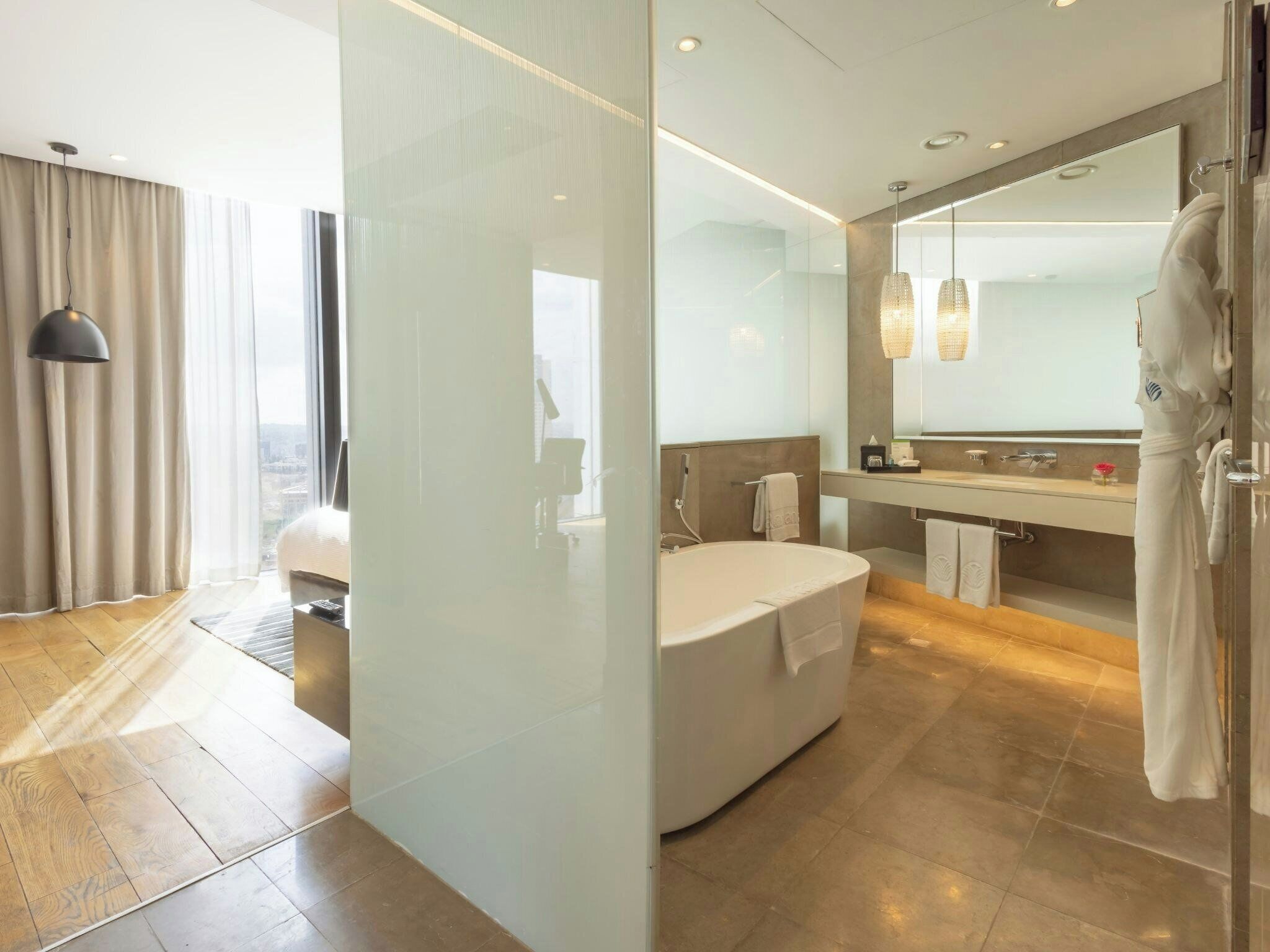 A modern bathroom with a bathtub, a large mirror, and a robe hanging on the wall.