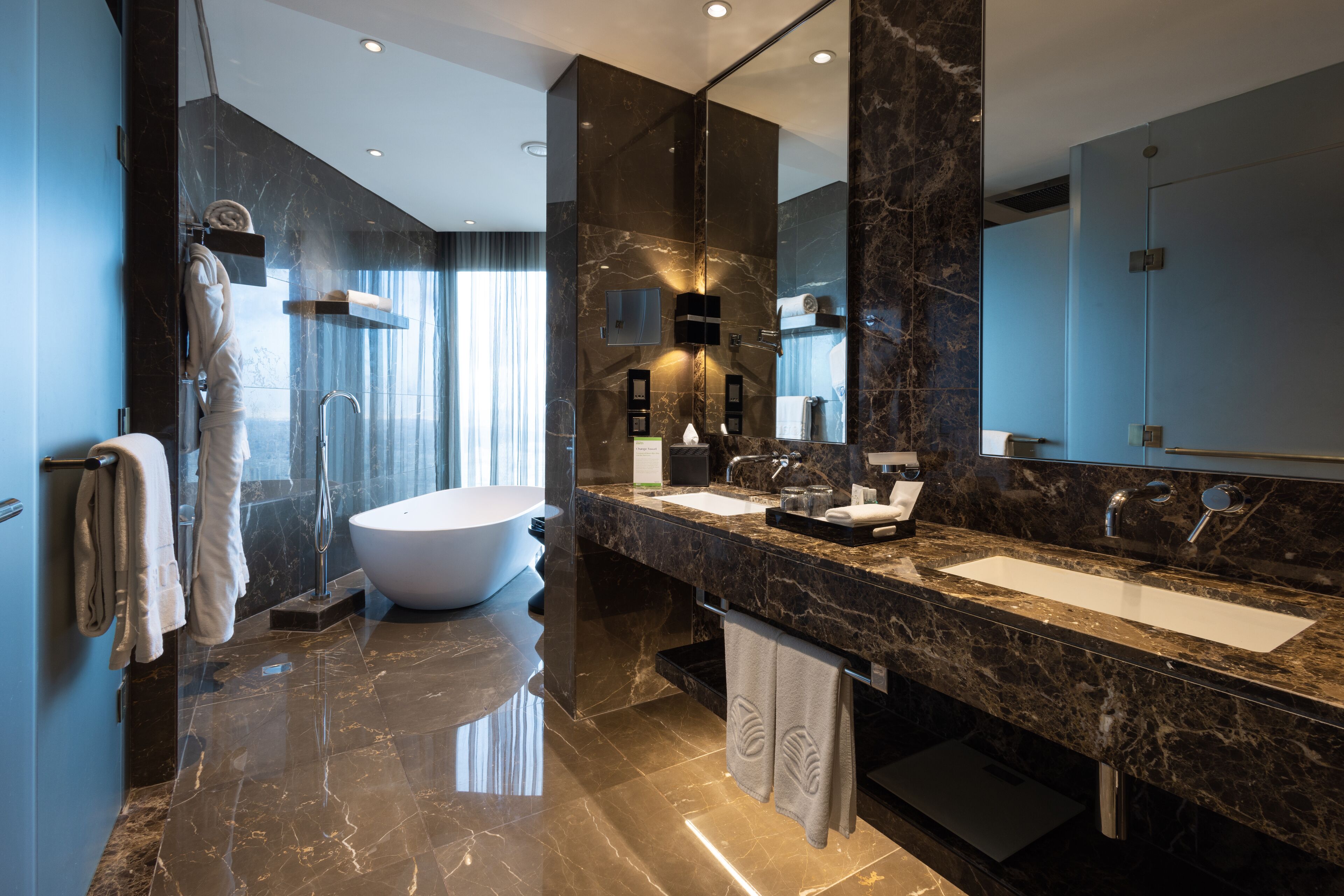 A modern bathroom with a freestanding bathtub, two sinks, and a large mirror.