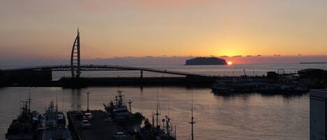 En lystbådehavn med fortøjede både, en bro i baggrunden og solnedgang over vandet.