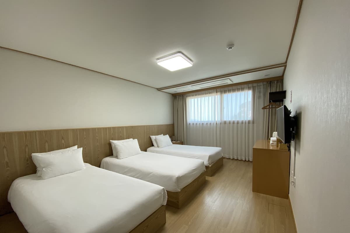 A hotel room with three single beds, a wooden headboard, a flat-screen TV, and a desk with a telephone.