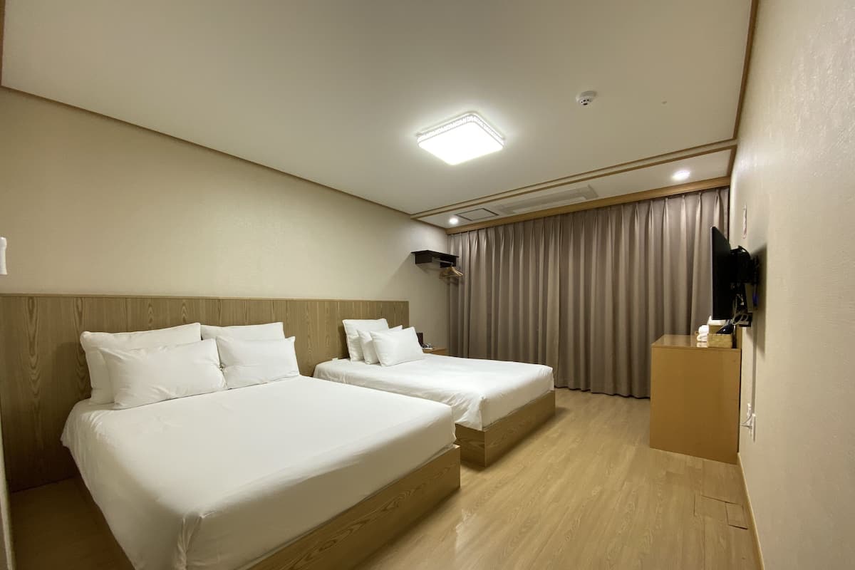 A hotel room with two beds, a wooden headboard, a flat-screen TV, and a desk with a computer.