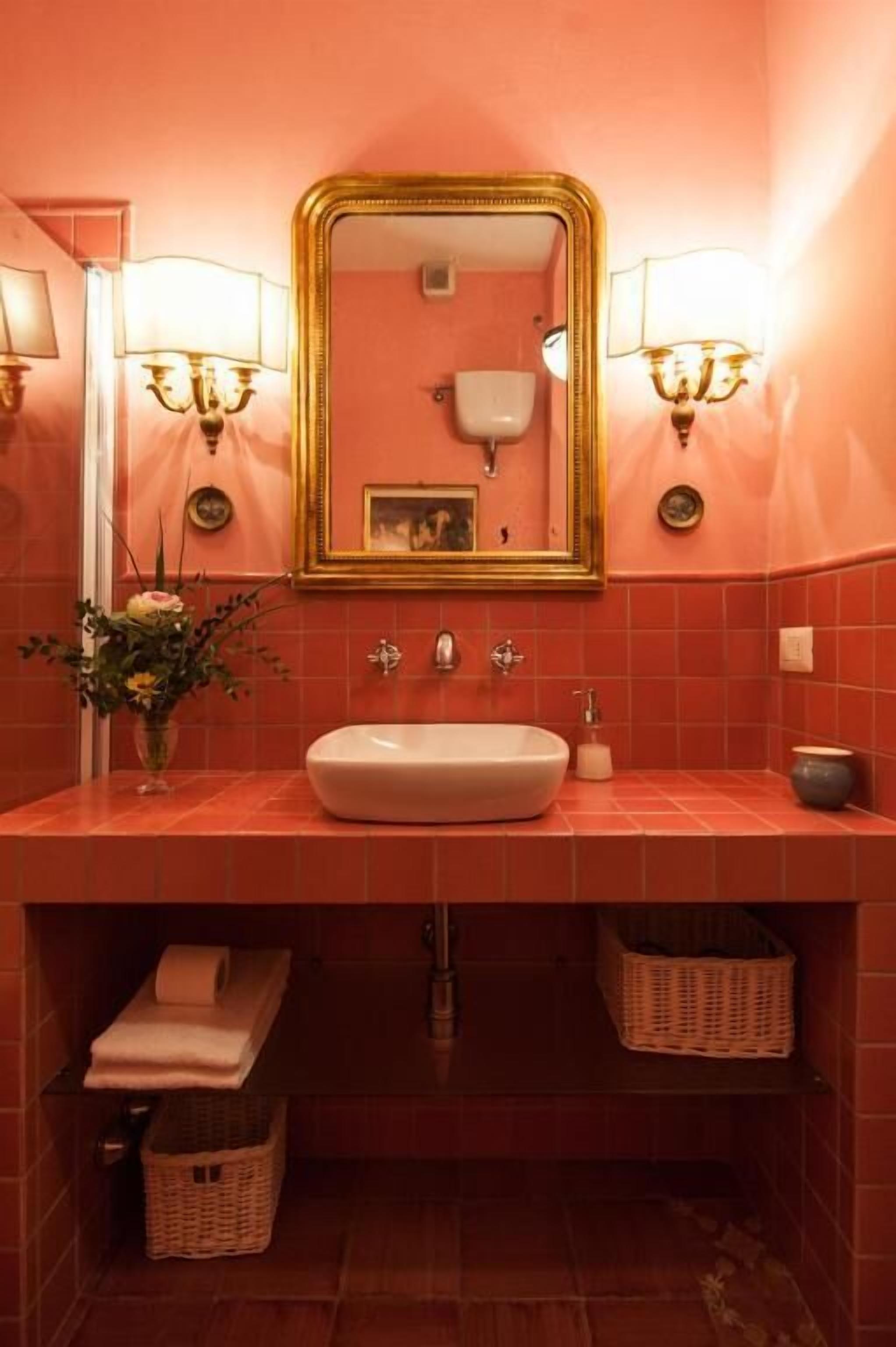 Un baño con un espejo grande, dos luces empotradas, un lavamanos y un florero con flores.