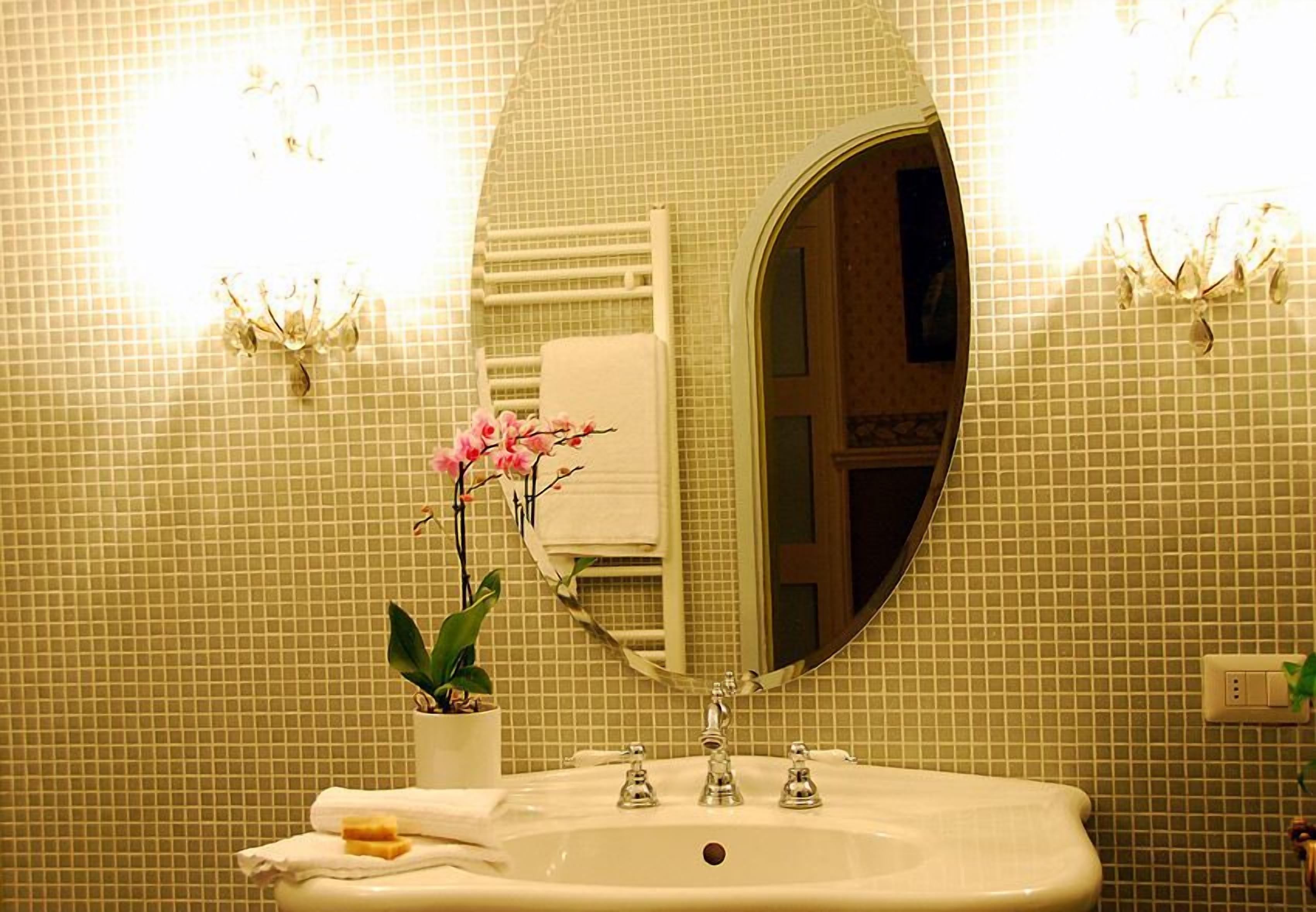 A bathroom with a white sink, a large mirror, and a potted orchid.