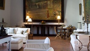 A spacious living room with a large painting on the wall, a white sofa set, a wooden coffee table, and a dining area with a table and chairs. - B&B Casa Schlatter (Florence)