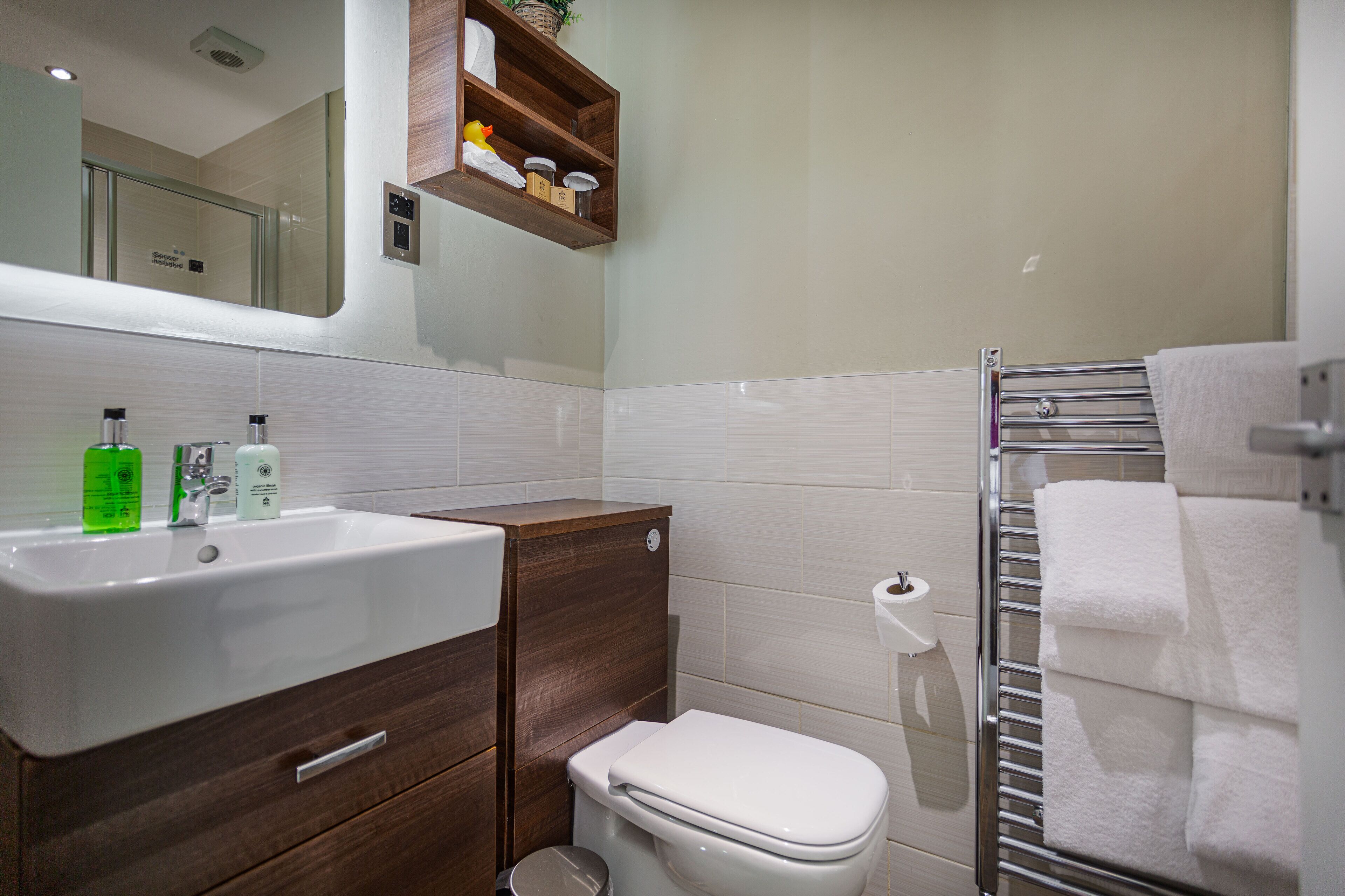 A bathroom with a white sink, wooden cabinet, white toilet, and a towel rack.