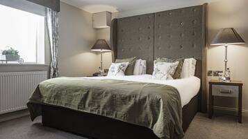 Een hotelkamer met een groot bed, twee nachtkastjes, een raam met gordijnen en een radiator.