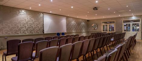 A conference room with rows of chairs, a whiteboard, and a patterned wall.