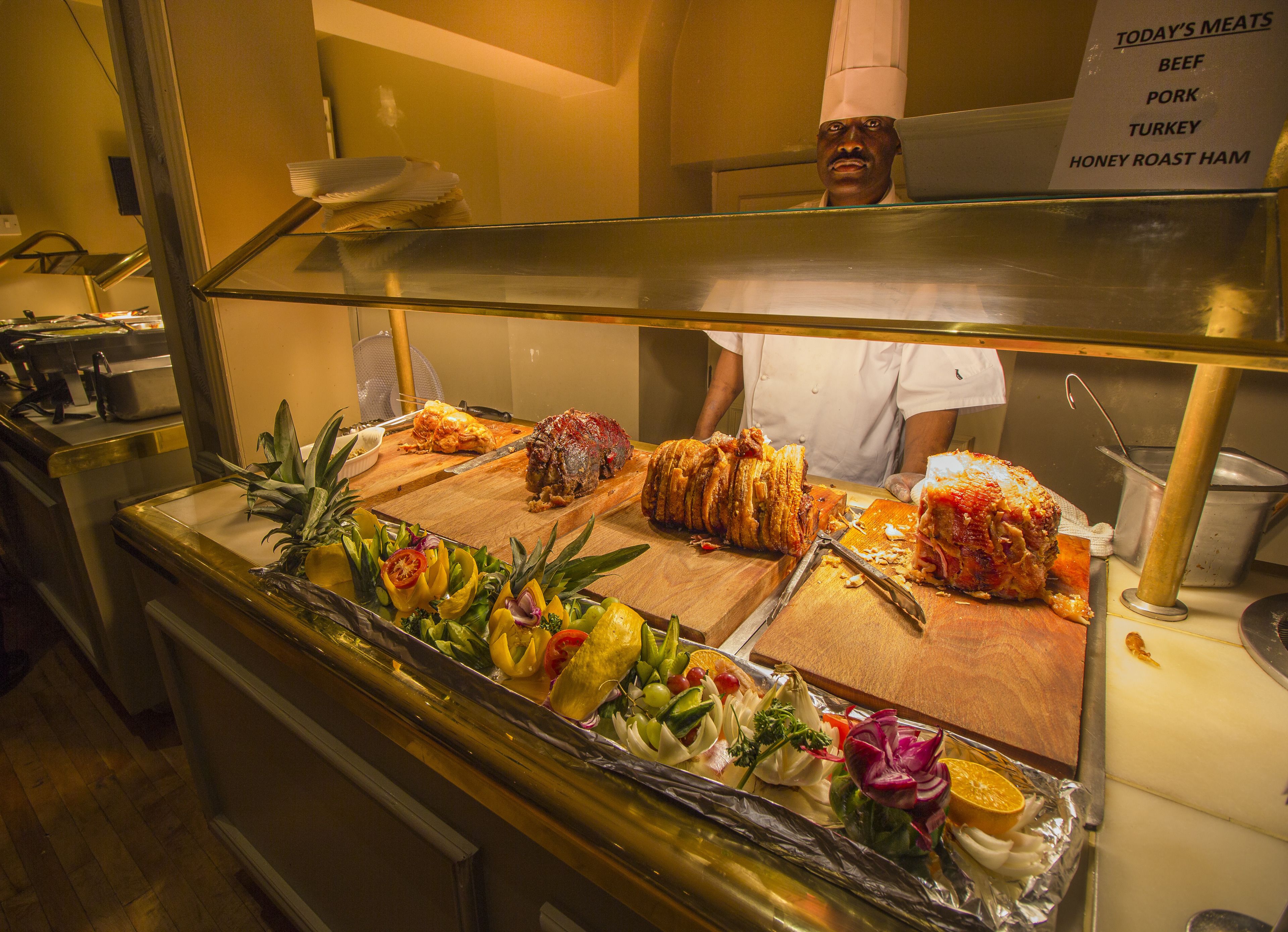 A buffet with various meats and a chef in the background.