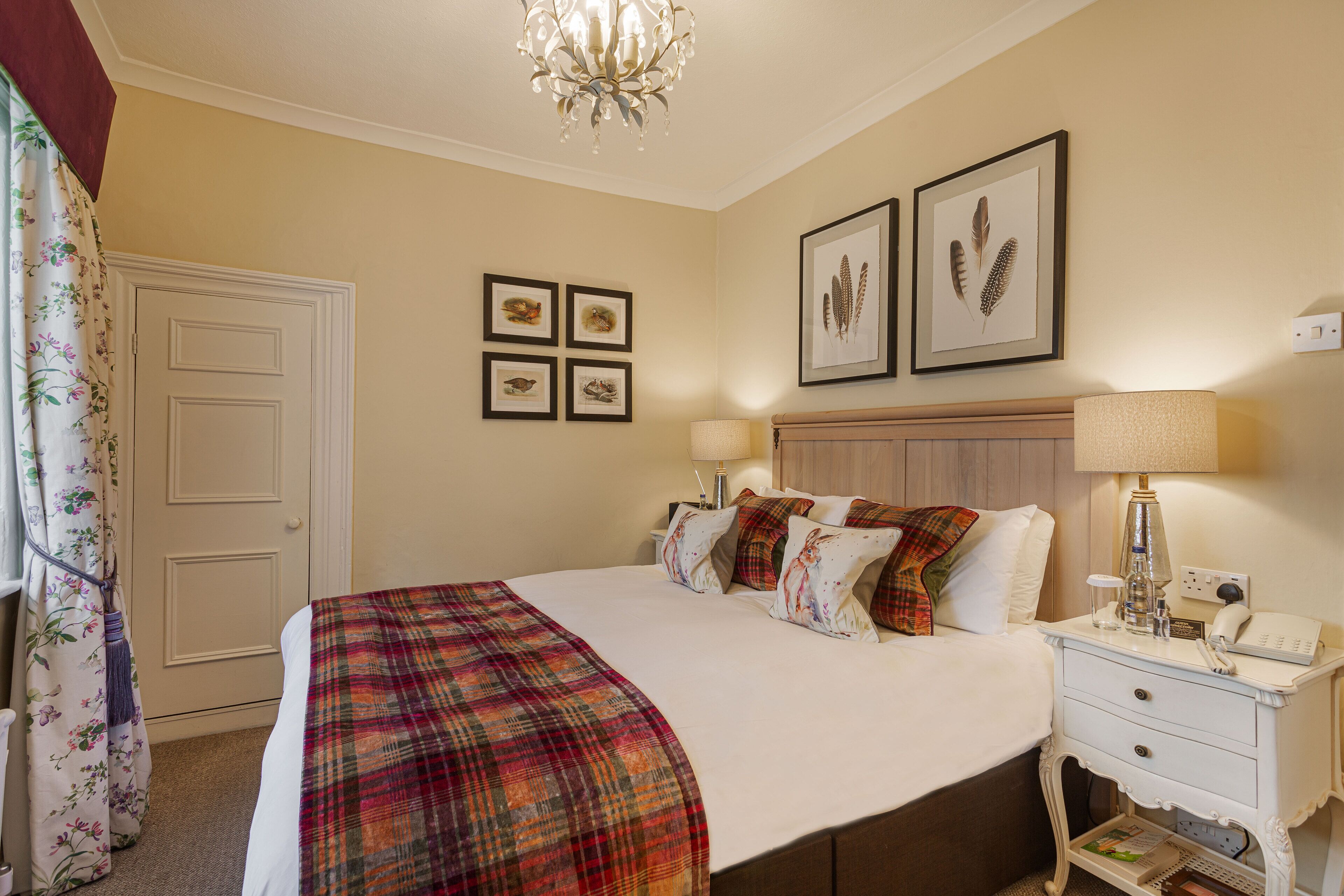 Un dormitorio ordenado con una cama grande, una mesita de noche con lámpara y una puerta con cortinas florales.