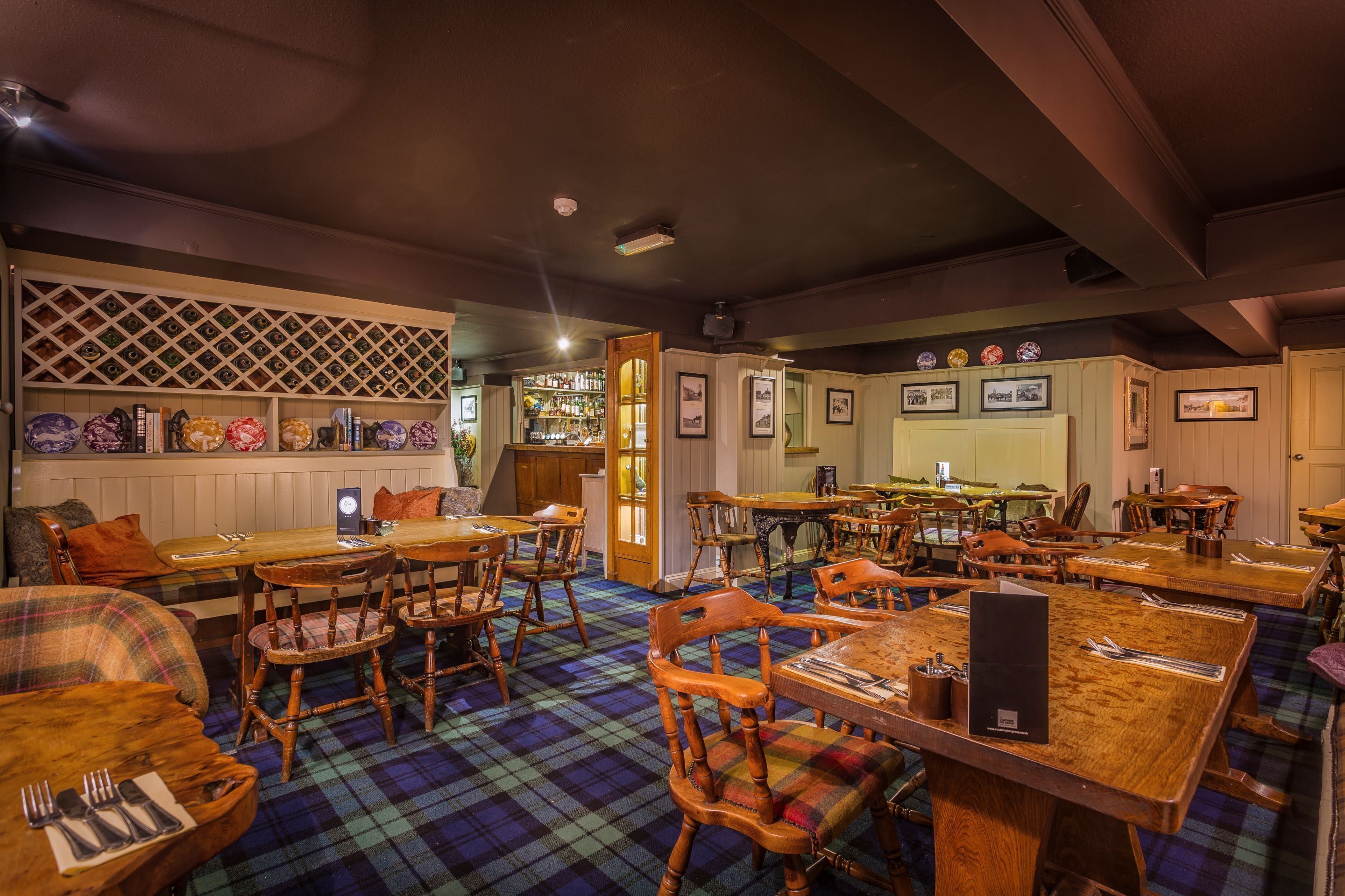 A restaurant with wooden tables and chairs, a checkered floor, and a bar area with shelves of bottles.