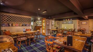 A restaurant with wooden tables and chairs, a checkered floor, and a bar area with shelves of bottles.