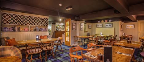 Un restaurante con mesas y sillas de madera, suelo a cuadros y una zona de bar con estantes llenos de botellas.