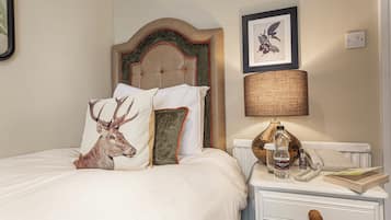 A bed with a deer head pillow, a lamp, a telephone, and a book on a bedside table.