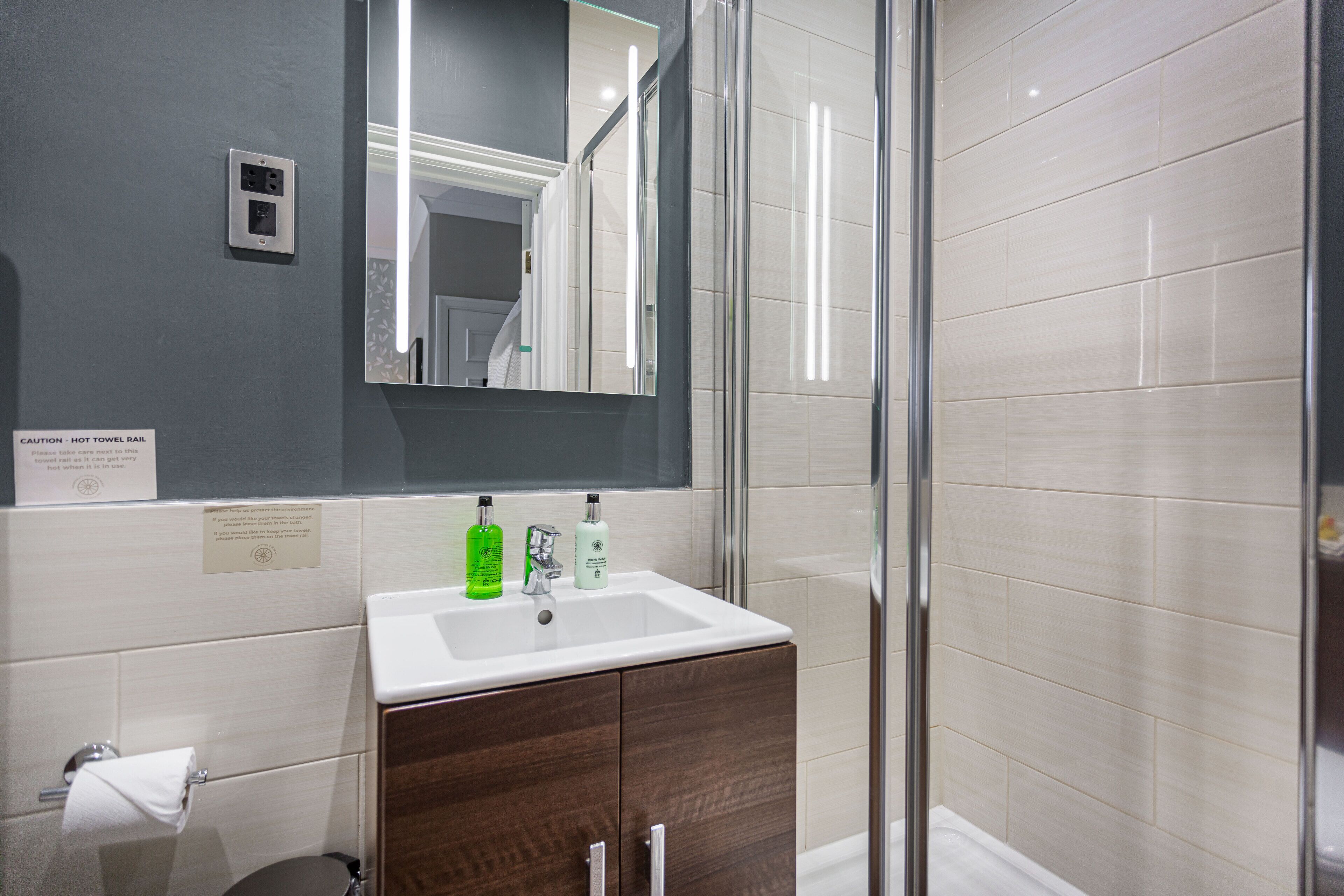 A modern bathroom with a white sink, dark wooden cabinets, a glass shower enclosure, and a large mirror.