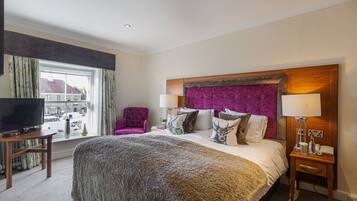 A hotel room with a large bed, a TV on a wooden table, a chair, and a window with a view of buildings.