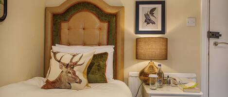 A neatly made bed with a headboard, a bedside table with a lamp, a framed picture on the wall, and a radiator.