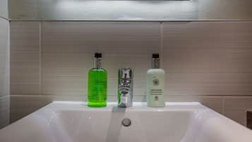 A bathroom sink with three bottles of liquid soap.