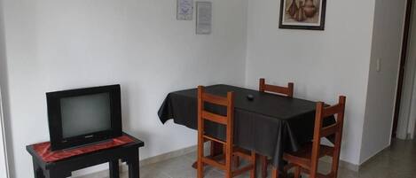 Ein kleiner Essbereich mit einem Tisch, vier Stühlen, einem Fernseher auf einem Schrank und zwei gerahmten Bildern an der Wand.